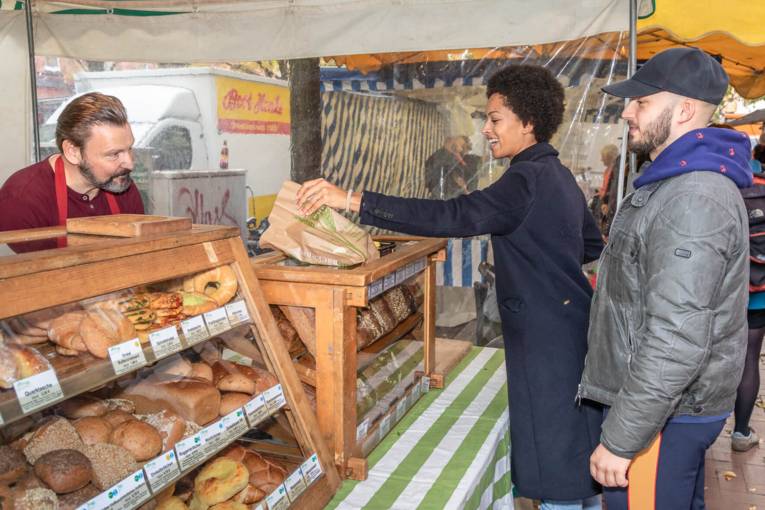 Eine Kundin kauft eine T&uuml;te mit Backwaren auf dem Marktstand eines B&auml;ckers.